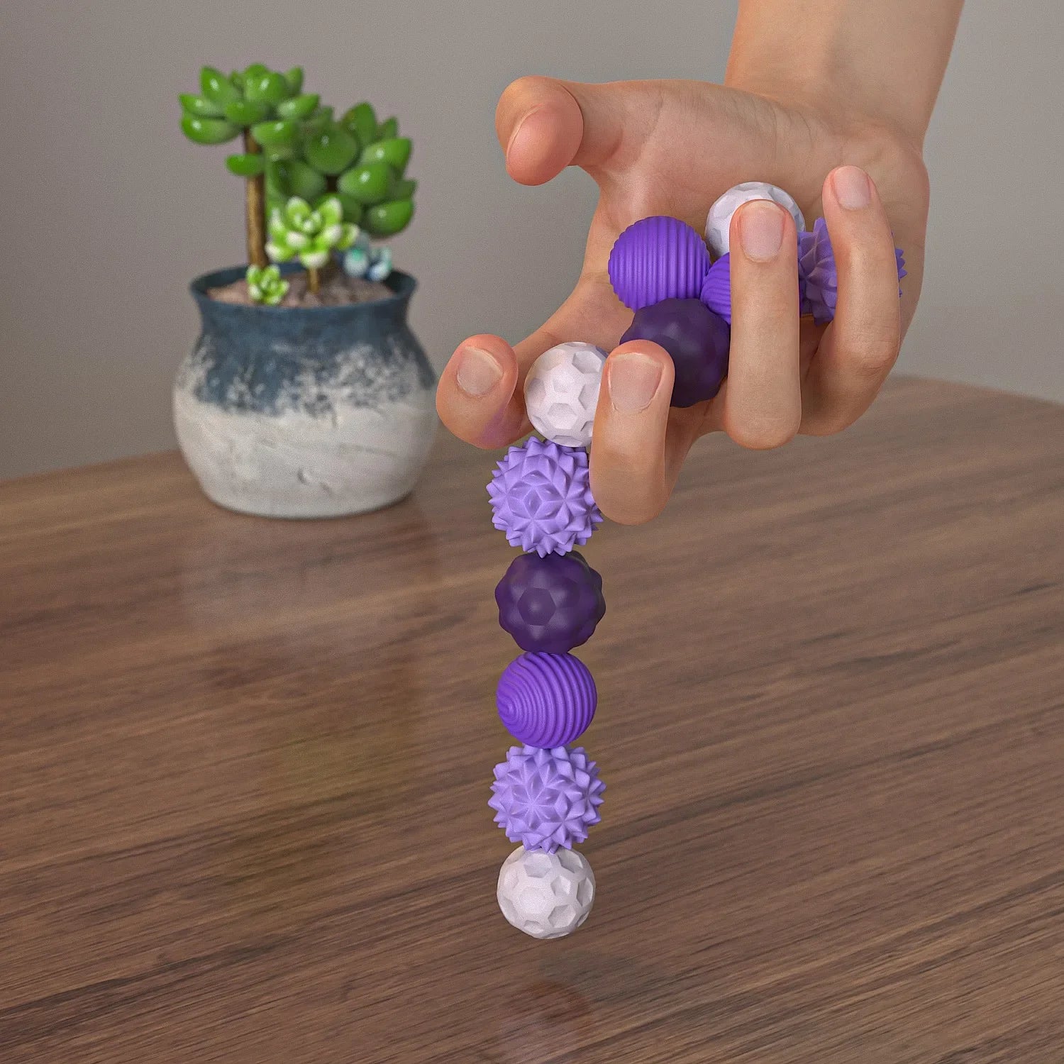 Hand holding a stack of purple and white textured balls on a wooden surface with a plant in the background.