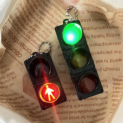 Close-up of a compact LED traffic light keychain attached to a backpack zipper.