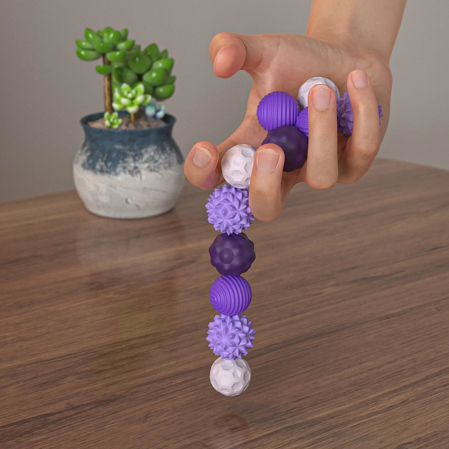 Hand holding a stack of purple and white textured balls on a wooden surface with a plant in the background.